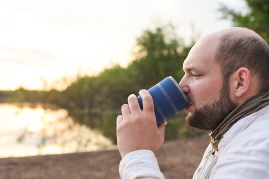 Hispanic man drinking a hot drink, coffee, on the bank of a stream at dawn. El Palmar National Park, Entre Rios, Argentina. - Powered by Adobe
