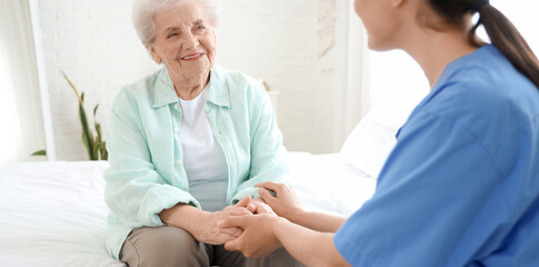 Physical therapist with senior woman holding hands in bedroom