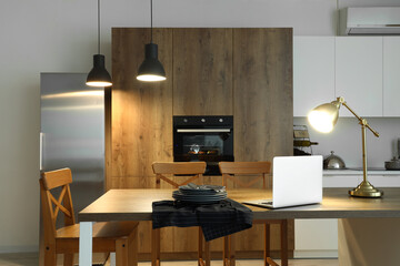 Interior of modern kitchen with glowing lamps and laptop on island table