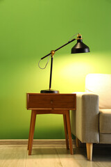 Glowing lamp on table and sofa near green wall in living room
