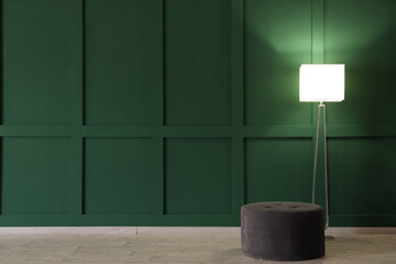 Glowing stand lamp with pouf near green wall in room