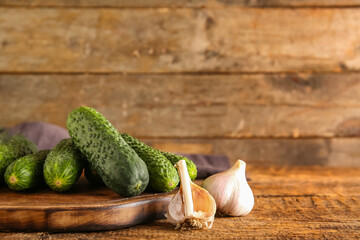 Board with fresh cucumbers and garlic on wooden background