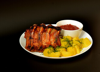 A plate of boiled potatoes, baked pork ribs with sauce on a black background.