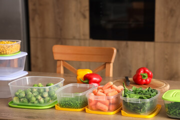 Plastic containers with vegetables for freezing on wooden table in kitchen