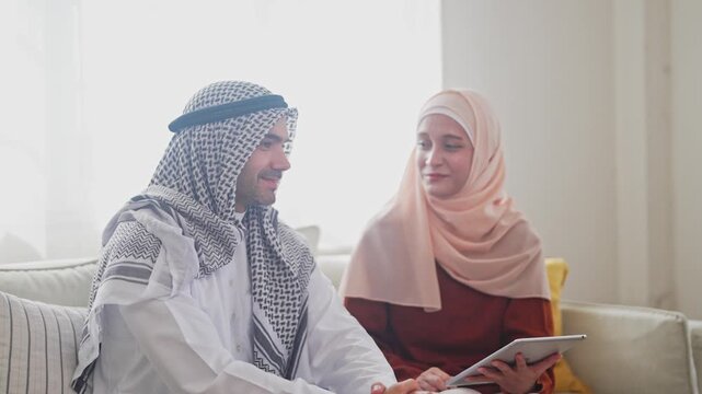 Muslim couple using tablet at home, modern islamic collaboration, learning or planning, concept of faith, family and technology online shopping, e-commerce platform, arab culture, islamic fintech