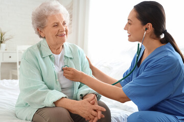 Obraz premium Physical therapist listening to senior woman with stethoscope in bedroom