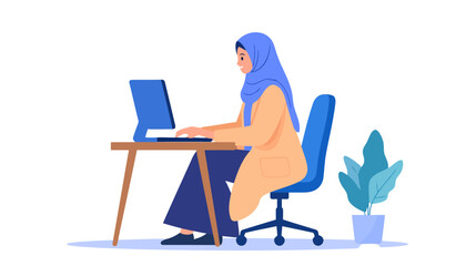 Young Muslim woman in a blue hijab and tan coat working diligently on a computer at her desk.
