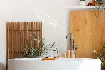 Interior of stylish bathroom with bathtub, board, laptop and houseplants