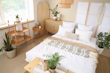 Comfortable bed, shelving unit, chest of drawers, bedside table and folding screen in interior of...