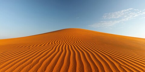 Naklejka premium Vast undulating orange sand dunes under a clear blue sky with sparse clouds