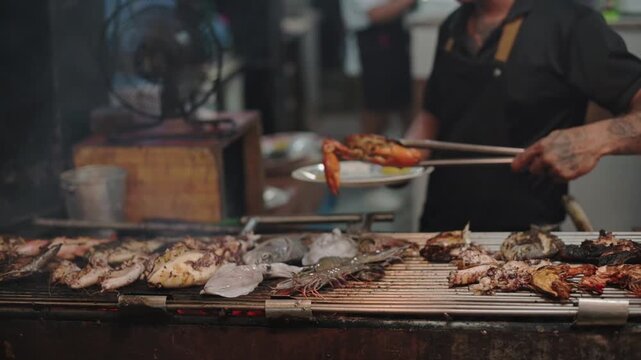 Assorted seafood including lobster and squid cooking on grill at El Nido night market, Philippines. Grilled seafood assortment with lobster claws and squid at street barbecue in El Nido, Philippines