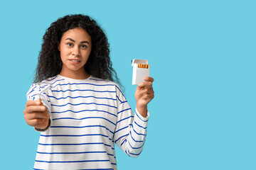 Young African-American woman with broken cigarette on blue background. Stop smoking concept