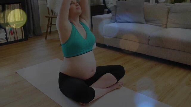 Pregnant woman placing hands on belly on yoga mat and lifting arms overhead for prenatal health