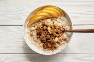 Bowl with tasty oatmeal, pieces of apple and nuts on white wooden background