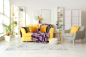 Interior of modern living room with armchair, shelving units and purple plaid on yellow sofa