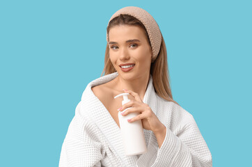 Pretty young woman in bathrobe with bottle of shower gel on blue background
