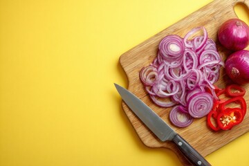 On a wooden board sliced red onions red peppers and a knife set against a yellow background