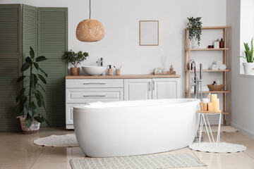 Interior of bathroom with bathtub, chest of drawers and folding screen