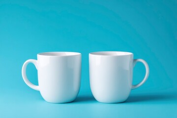 Two white ceramic mugs sit on a light blue surface against a matching backdrop