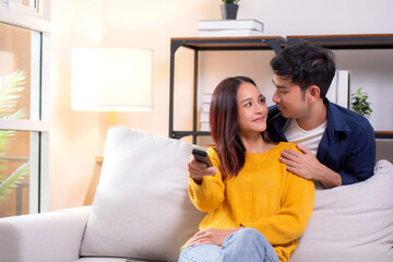 Happy young asian couple sitting on cozy sofa watching TV together and enjoying a relaxation in...
