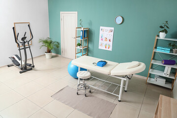 Interior of physiotherapist's office with couch, shelf units and exercising bike