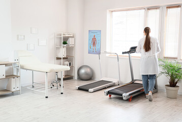 Obraz premium Female physiotherapist near treadmill in office, back view