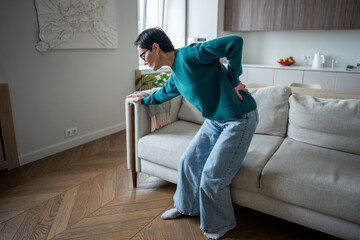 Senior woman gripping lower back in severe pain from sudden spinal attack. Slipped disc, arthritic...