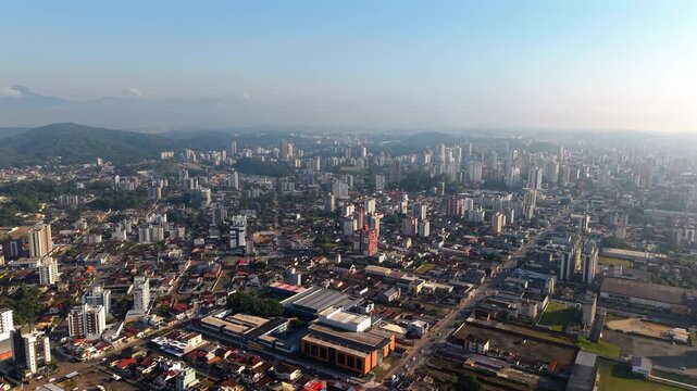 Drone ascends and pulls away from Joinville, Santa Catarina, Brazil, unveils the turquoise waters of Babitonga Bay, the forested Serra do Mar coastal mountains, dense urban grid and Atlantic horizon.