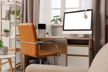 Workplace with blank computer monitor and green plants near window in office