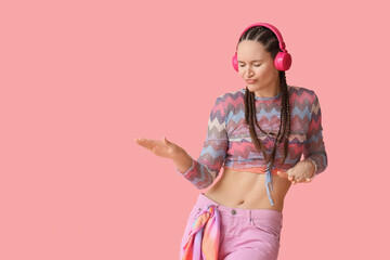 Fashionable young woman in headphones with dreadlocks dancing on pink background
