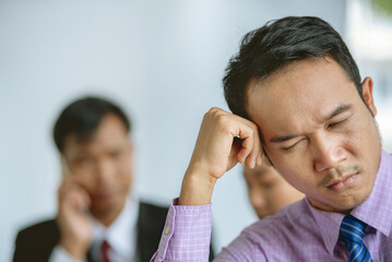 A man in a purple shirt and tie is sitting with his hand on his head looking stressed while his...