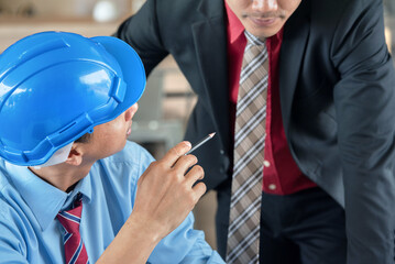 Two businessmen in hard hats and suits discuss plans while looking at blueprints.