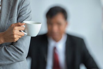 A business woman holding a cup of coffee with a blurred background of a businessman