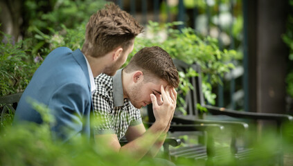 A man is comforting his friend who is crying on a park bench.
