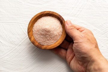 Hand holding a bowl of pink Himalayan salt: exotic cooking ingredient