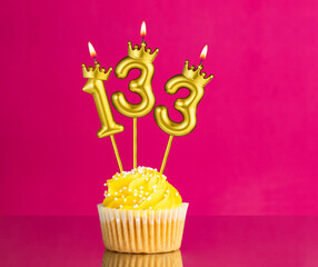 Birthday celebration with number 133 candle - Yellow cupcake on a pink background
