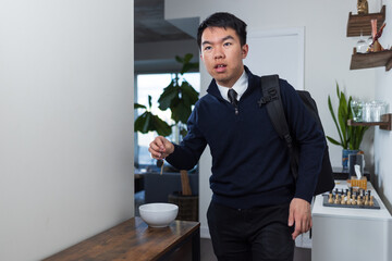 A young man dressed for work picks up his keys while wearing a backpack. The image captures morning...