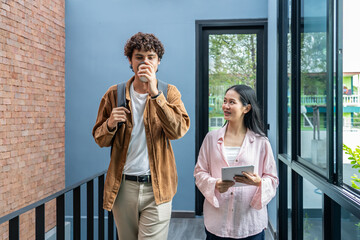 Two happy friendly young diverse business people talking during work break walking in office, caucasian and asian couple employees share ideas enjoy conversation discussing team project at meeting