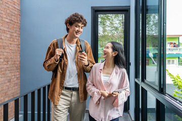 Two happy friendly young diverse business people talking during work break walking in office, caucasian and asian couple employees share ideas enjoy conversation discussing team project at meeting