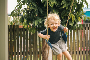 Happy little boy with big smile on backyard swing