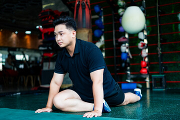 Fototapeta premium Young Asian man stretching during a workout session in a modern gym environment