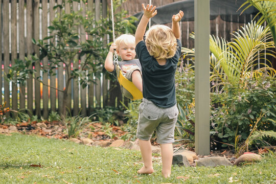 Small boy pushing little brother on backyard swing - Powered by Adobe