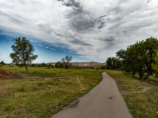 A paved path in the middle of a grassy field under a cloudy sky