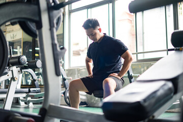 Asian man resting on a gym bench after a workout session in a fitness center during daytime