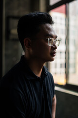 Man in glasses looks thoughtfully out the window, reflecting on life in a quiet urban space during the late afternoon