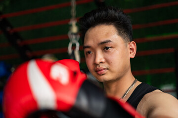 Young Asian male boxer preparing for training in a gym, focusing on technique with boxing gloves in...