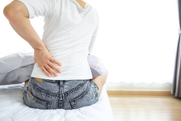 Woman holding her lower back while sitting in bed has chronic back pain. Medical and healthcare concept