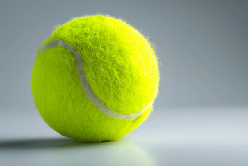 A bright yellowgreen tennis ball sits on a white surface in a studio shot