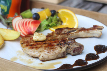 A delicious grilled pork chop served with garlic, brown sauce, and sides of potato