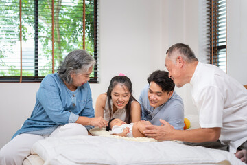 Joyful Asian Family Bonding with Their New Baby at Home, Grandparents and Parents Looking at Infant...